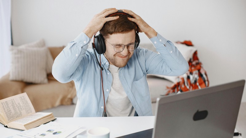 A frustrated man with headphones working at home office, laptop on desk., tags: selbstständige - pexel