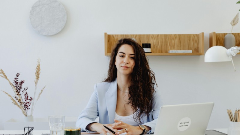 Businesswoman in a light blazer sitting at a desk with a laptop, exuding confidence in a modern office., tags: selbstständigkeit richtig absichern: - pexel