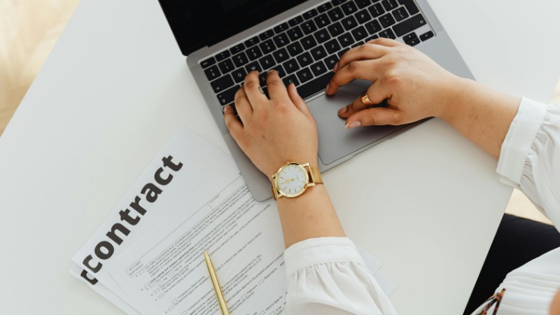 A woman using a laptop alongside a contract document on a desk, emphasizing business and legal themes., tags: freelancer und startups - pexel